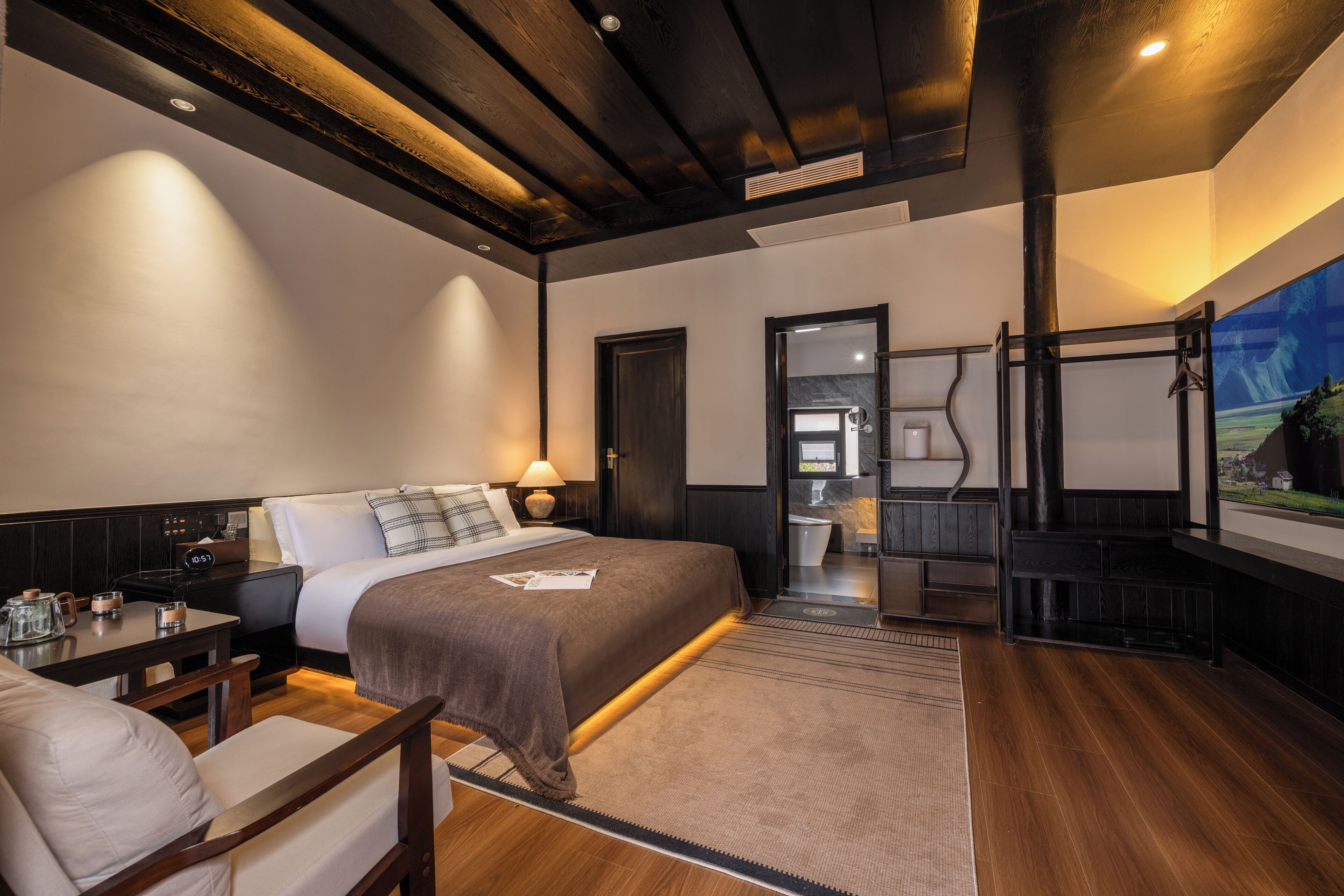 A modern hotel room with a large bed, a desk, a chair, a nightstand, and a bathroom visible through an open door.