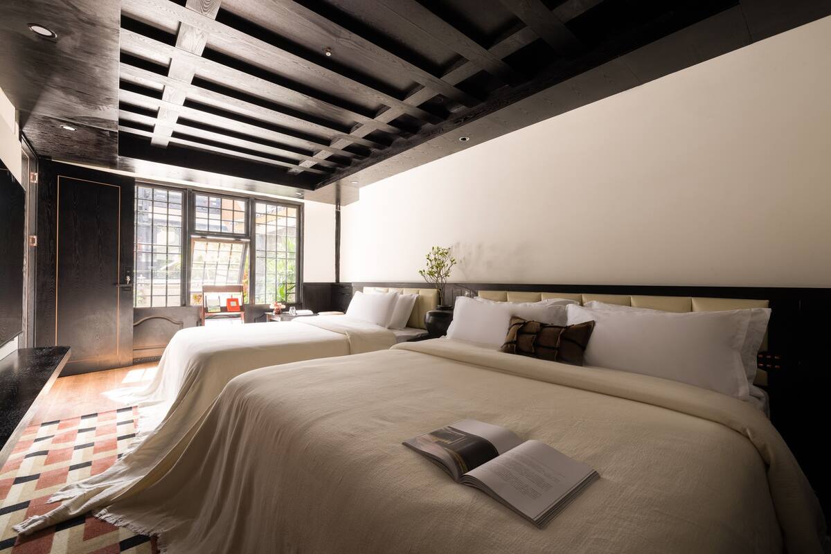 Habitación de hotel con dos camas, un ventanal grande y techo de madera.