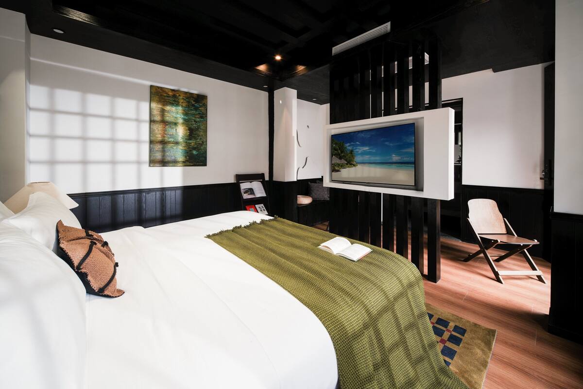 Una habitación de hotel moderna con una cama grande, un televisor de pantalla plana, un escritorio pequeño y vistas a la playa.