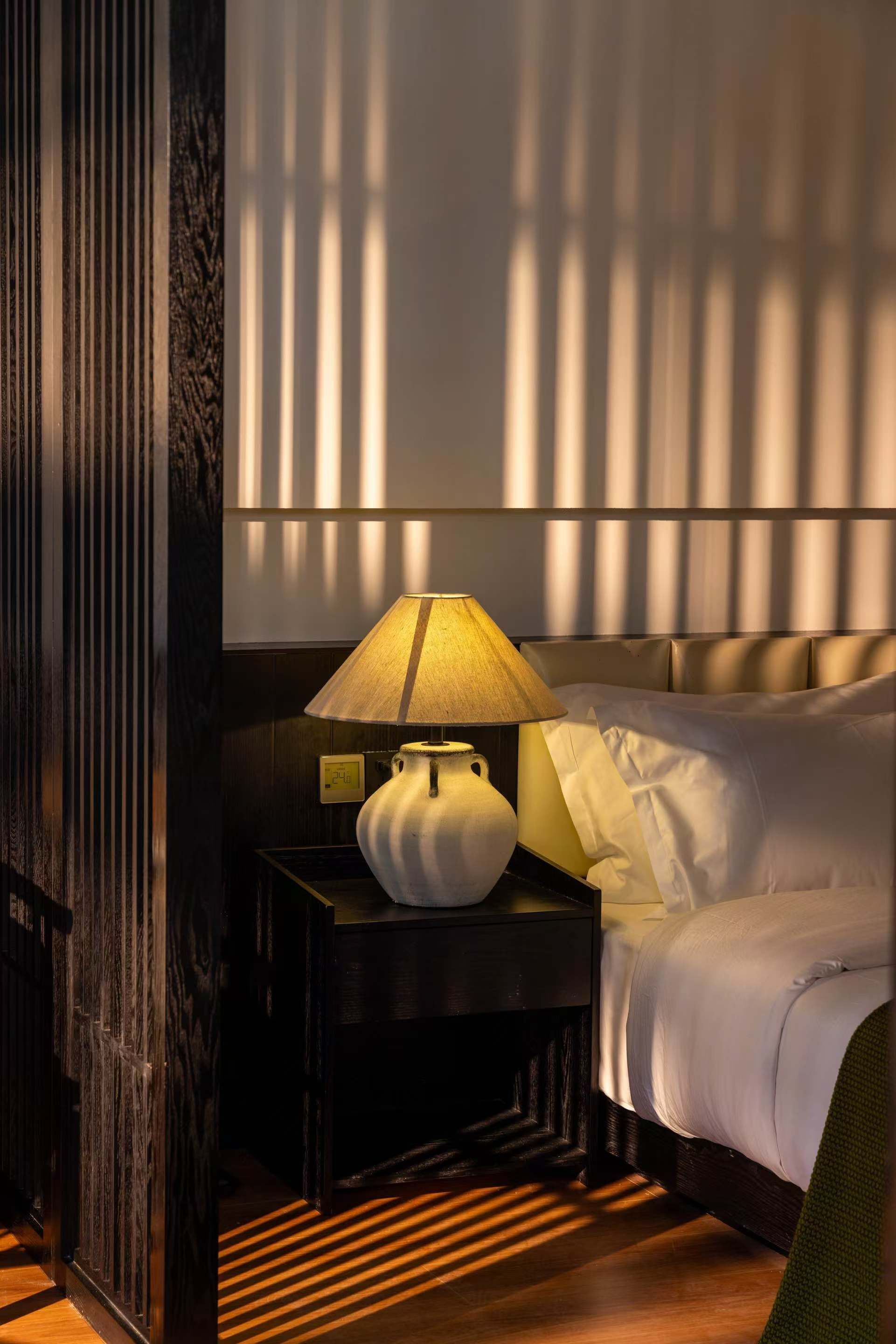 Una habitación de hotel con una cama, una mesita de noche con lámpara y una ventana con persianas.