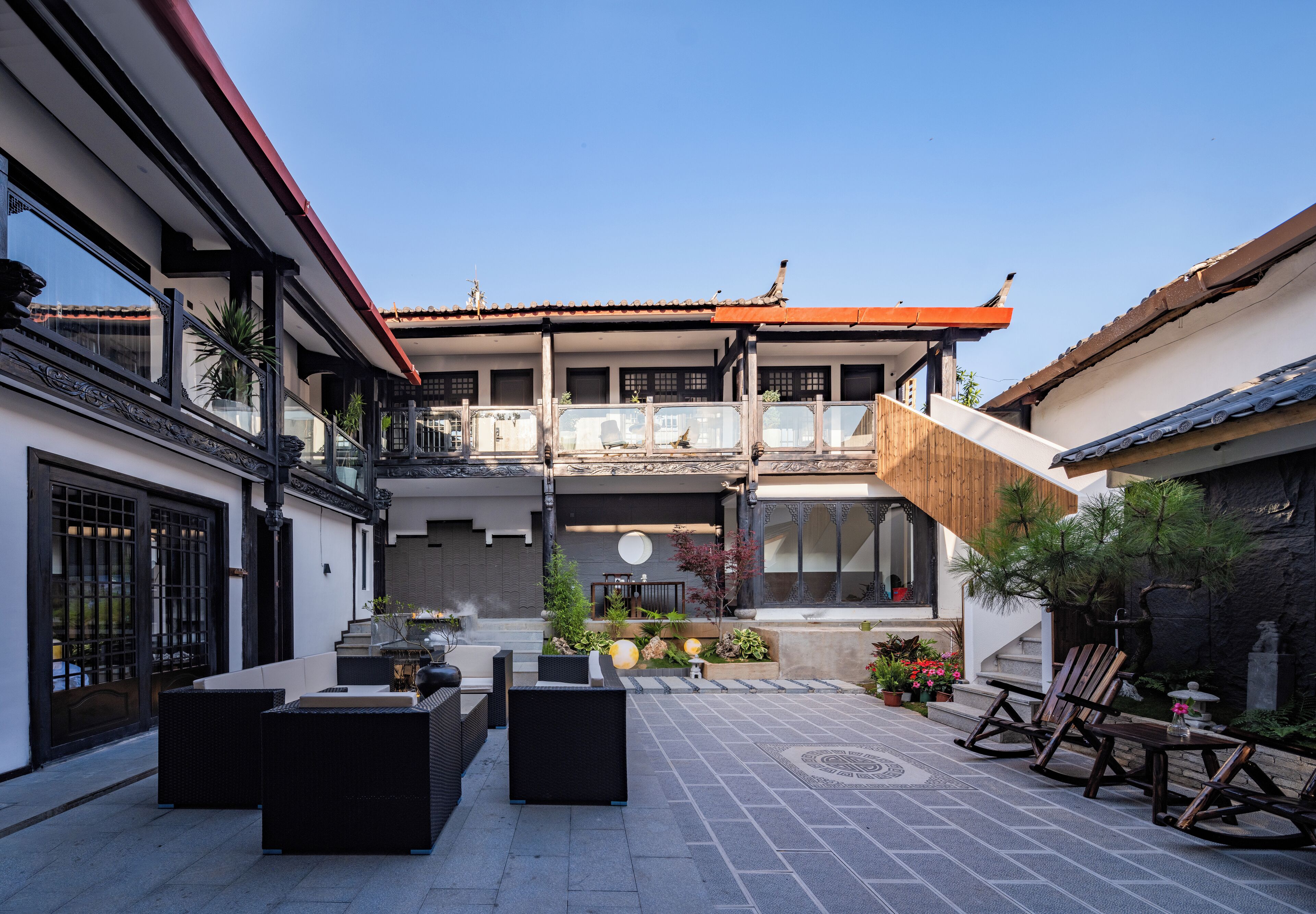 A courtyard with outdoor seating, a wooden staircase, and a traditional building with a tiled roof.