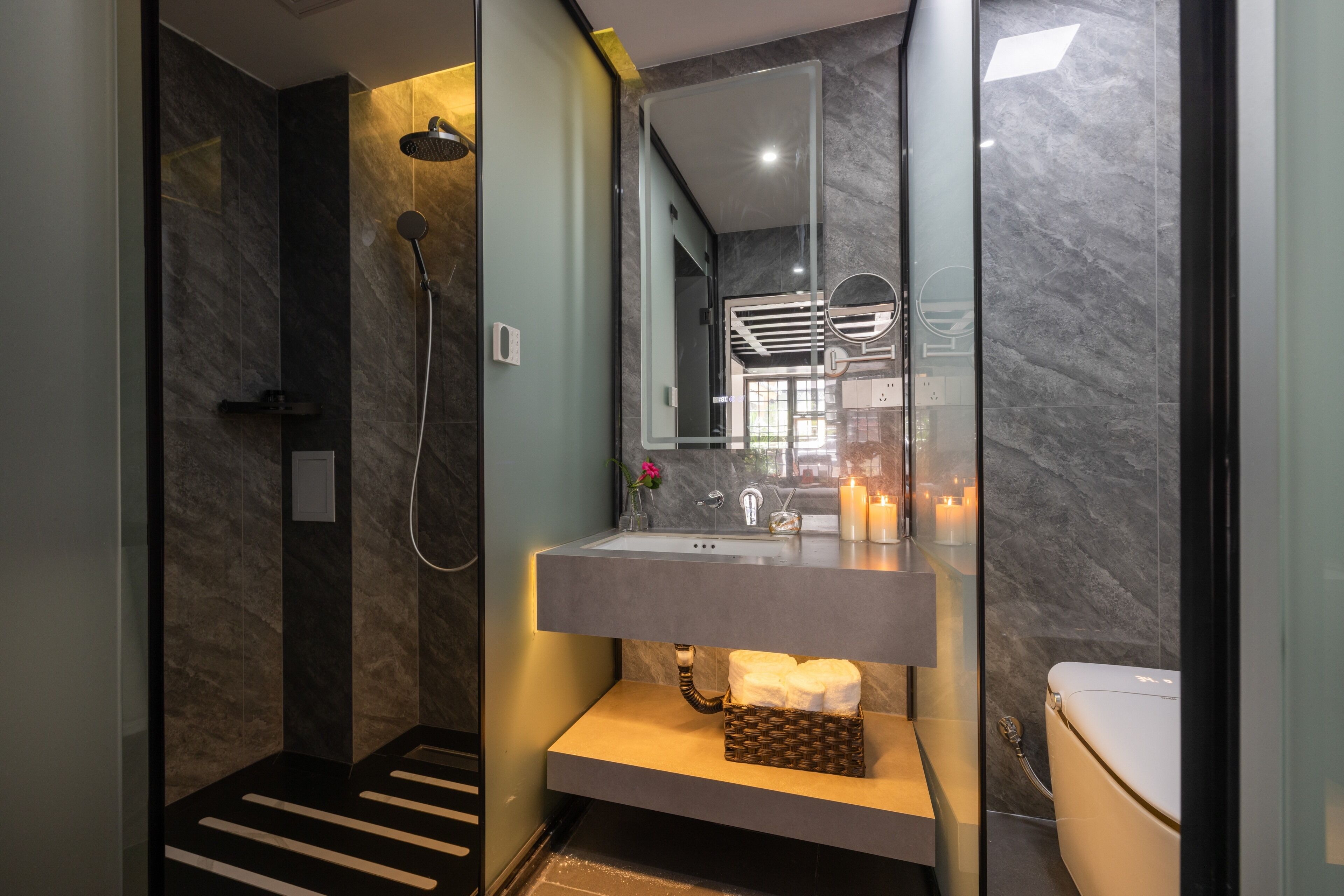 A modern bathroom with a glass-enclosed shower, a marble-tiled wall, a built-in sink, and a toilet.