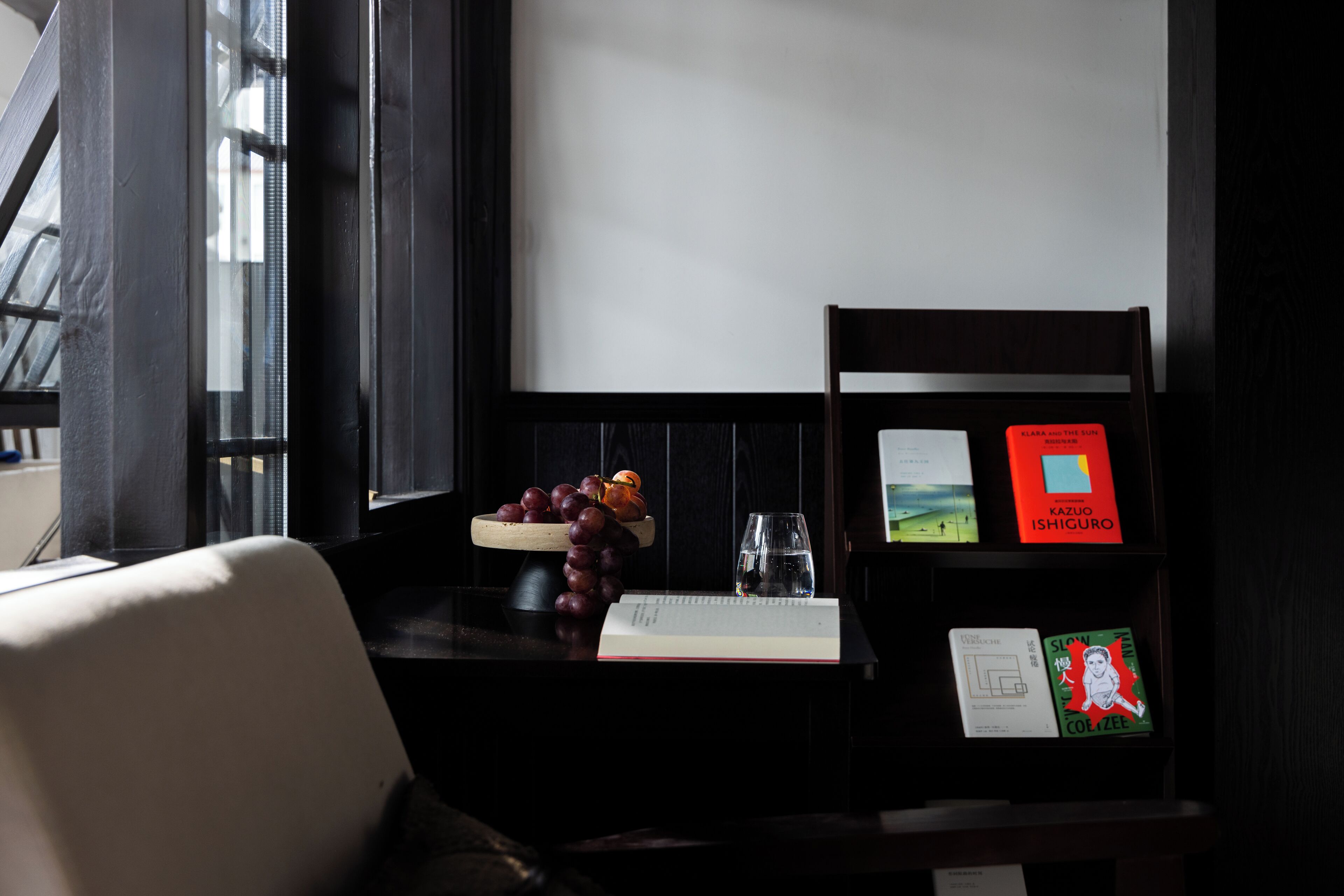 A dark wooden desk with a bowl of grapes, a glass of water, and books.