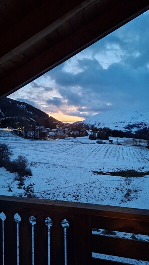 A snowy landscape with a wooden deck and a view of a village in the distance. - Le Refuge du Loup - Panoramic Views, Netflix, and a Pool (Dévoluy)