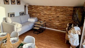 A cozy living room with a grey sofa, a small table, and a wooden wall. There are framed pictures on the wall and a Christmas tree on the floor. - Le Refuge du Loup - Panoramic view, Netflix & Pool (Dévoluy)