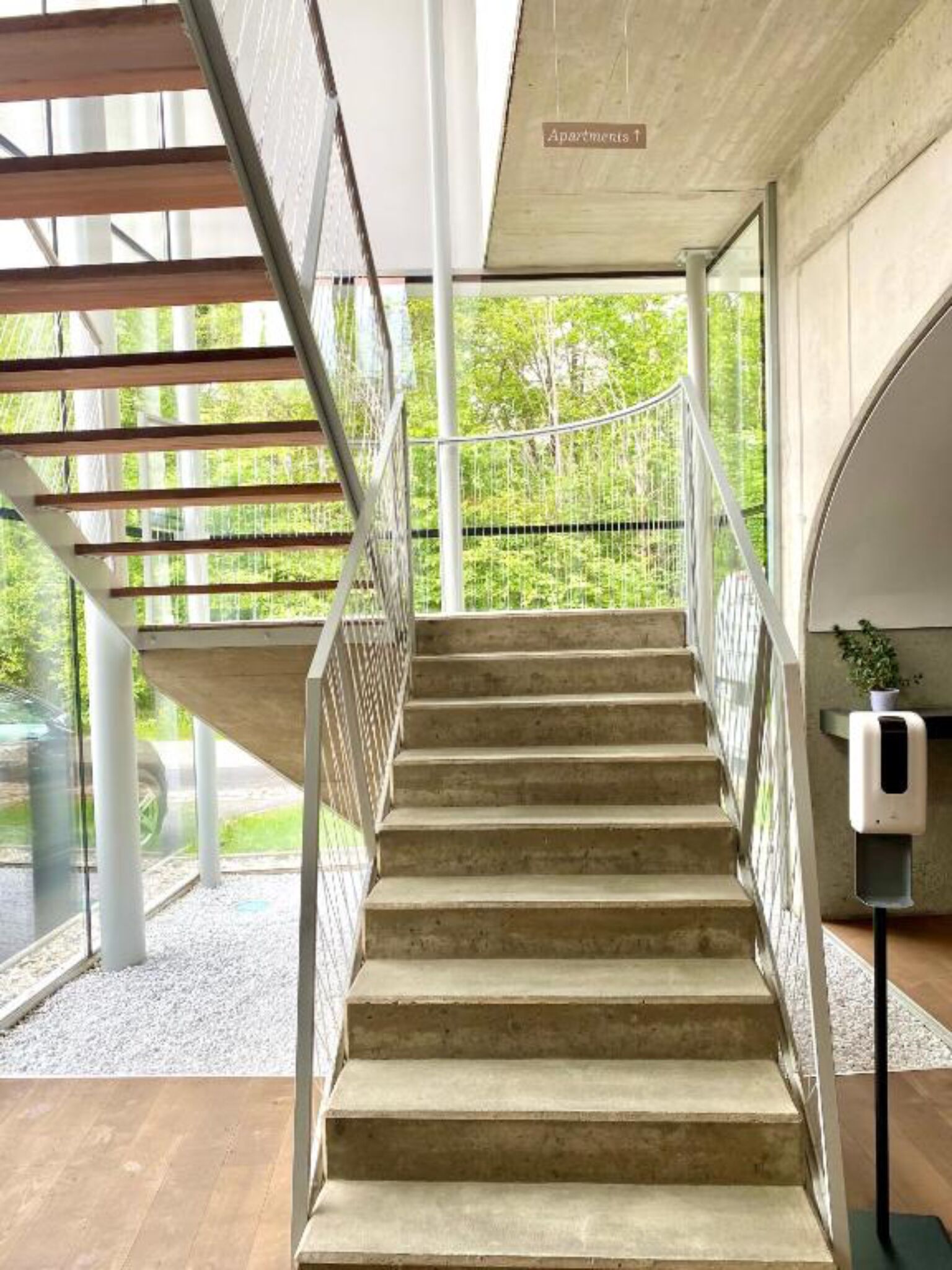 Un escalier avec une rampe en métal menant à un niveau supérieur, entouré de grandes fenêtres offrant une vue sur la verdure.