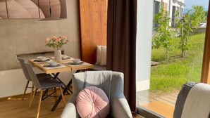 A modern living room with a grey armchair, a wooden dining table set, and a view of a garden through large windows. - At home in the location with pool in beautiful surroundings (Graßnitzberg)