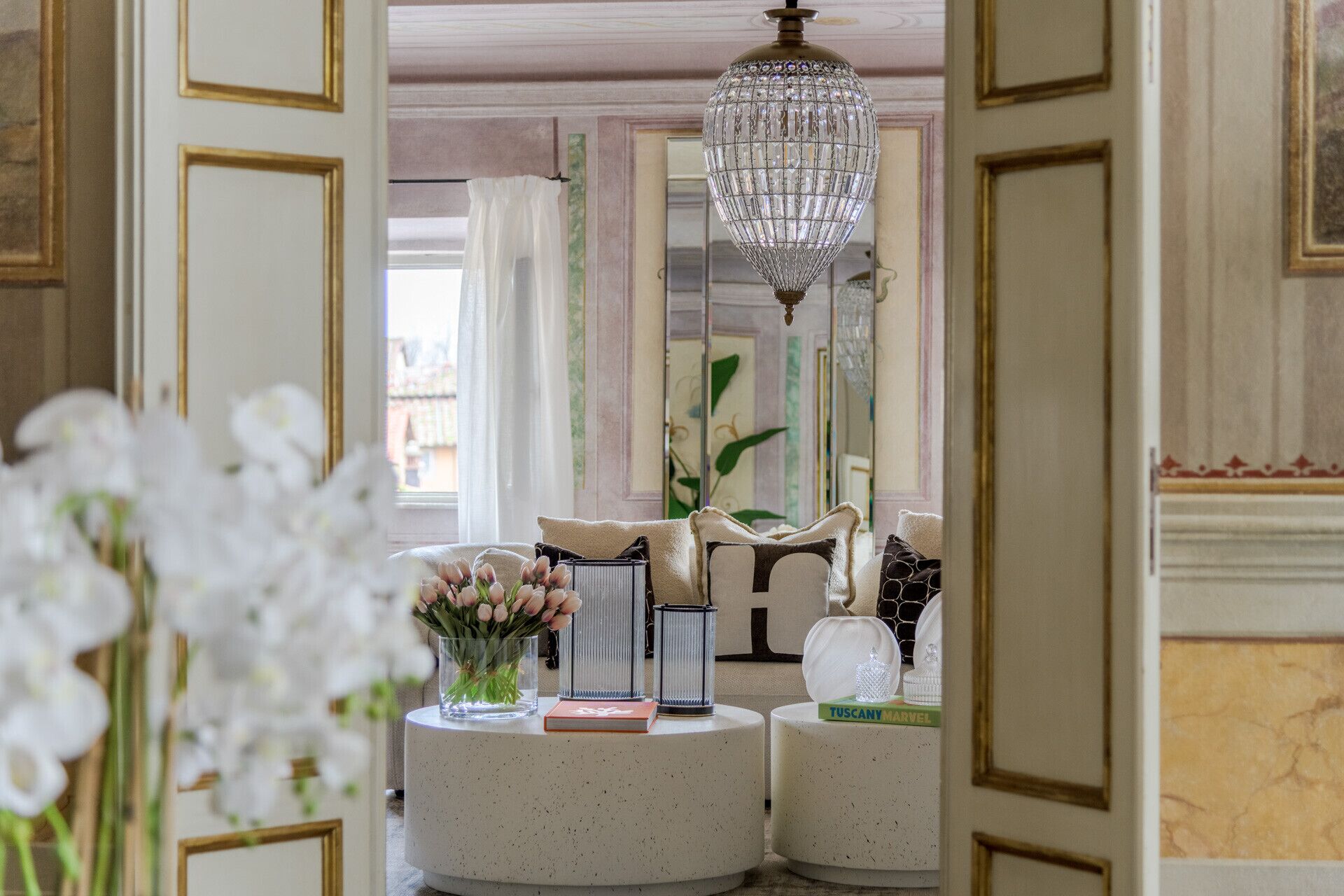 A room with a round table, a chandelier, and a mirror.