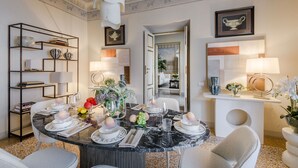 A dining area with a round table set for four, surrounded by chairs. There is a bookshelf with books and decorative items, a large mirror, and a framed picture on the wall. - The Marble Penthouse (Lucca)