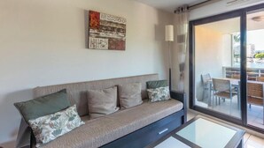 A modern living room with a sofa, a glass coffee table, and a view of an outdoor dining area through a sliding glass door. - nice Apt for 6 pers near the Marina (Mandelieu-la-Napoule)