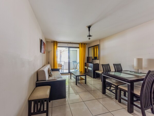 A modern living room with a sofa, a dining table with chairs, a TV, and a ceiling fan. - Nice apart for 4pers, close to the marina (Mandelieu-la-Napoule)