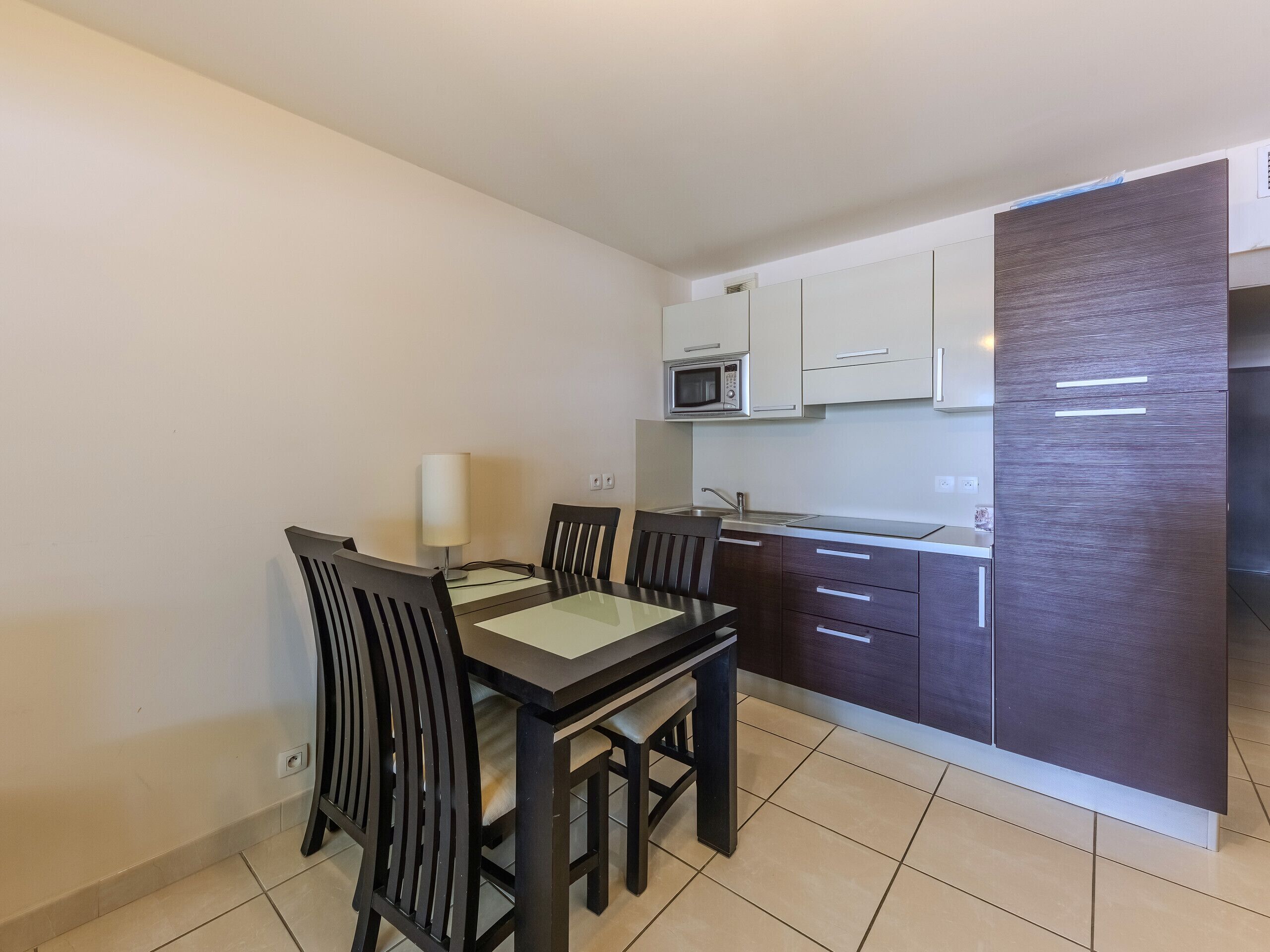 A compact kitchen with white cabinets, a microwave, and a dark-colored refrigerator.