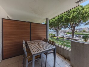 A balcony with a wooden table and chairs, a view of a marina, and a large tree. - Nice apart for 4pers, close to the marina (Mandelieu-la-Napoule)