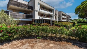 Um edifício moderno de vários andares com varandas, rodeado por jardins bem cuidados e um céu claro.