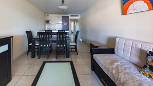 Uma sala de estar moderna com um sofá, uma mesa de jantar com cadeiras e uma cozinha ao fundo.