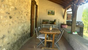 Um alpendre coberto com uma mesa e cadeiras de madeira, uma parede de pedra e uma pintura na parede.