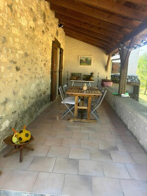 Eine überdachte Terrasse mit einem Holztisch und -stühlen, einer Steinmauer und einem Bild an der Wand.