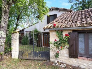 Ein rustikales Steinhaus mit Ziegeldach, einem Metallgitter und einem kleinen Garten mit roten Blumen.