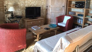 Um quarto acolhedor com parede de pedra, um armário de madeira, uma televisão, uma estante, uma cadeira de vime vermelha, uma mesa de madeira e uma cama.