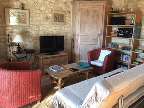 Ein gemütlicher Raum mit Steinwand, Holzschrank, Fernseher, Bücherregal, rotem Korbstuhl, Holztisch und einem Bett.