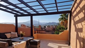 A covered outdoor seating area with a view of mountains and palm trees. - Holiday Home 'Fantastic Townhouse Aloha Na' with Mountain View, Wi-Fi and Air Conditioning (Marbella)