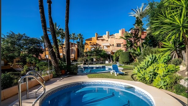 A swimming pool with a geometric tile pattern, surrounded by palm trees and greenery, with a building in the background. - Holiday Home 'Fantastic Townhouse Aloha Na' with Mountain View, Wi-Fi and Air Conditioning (Marbella)