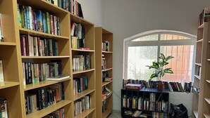 A library with wooden bookshelves filled with books, a potted plant, and a window with a view. - Holiday Home 'Fantastic Townhouse Aloha Na' with Mountain View, Wi-Fi and Air Conditioning (Marbella)