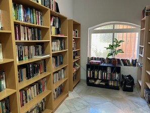 A library with wooden bookshelves filled with books, a potted plant, and a window with a view. - Holiday Home 'Fantastic Townhouse Aloha Na' with Mountain View, Wi-Fi and Air Conditioning (Marbella)