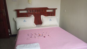 A bed with a pink quilted bedspread, two white pillows with a logo, and a wooden headboard.