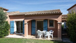 A house with a patio, a dining area with white chairs, and a blue door. - Air-conditioned house for 6 people with garden and swimming pool near the lake (Homps)
