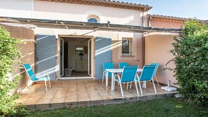 Eine Terrasse mit blauen Stühlen und einem Tisch, eine Tür, die in den Innenraum führt, und ein Ziegeldach.