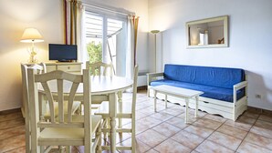 A room with a dining table, chairs, a blue sofa, a TV, and a lamp. - South-facing villa for 6 people with a garden and swimming pool (Homps)