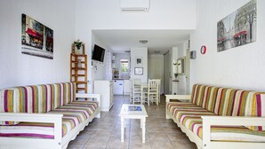 Een woonkamer met twee gestreepte banken, een salontafel, een televisie en een keuken op de achtergrond.