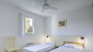 Een kamer met twee eenpersoonsbedden, een stoel, een plafondventilator, een raam en een wandlamp.