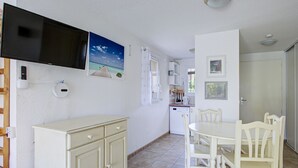 Een kleine keuken met een eethoek, witte kasten en een wandgemonteerde flatscreen televisie.