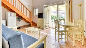 A living room with a sofa, a dining table with chairs, a TV, a fan, a staircase, and a sliding glass door leading to an outdoor area. - Charming villa with garden for 6 pers (Homps)