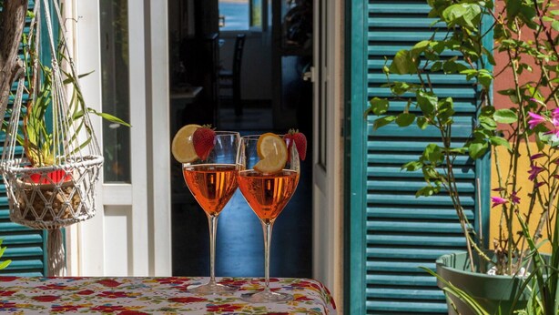 Una mesa con dos vasos de líquido ámbar, posiblemente vino, adornada con rodajas de fruta, sobre un mantel estampado con motivos florales.