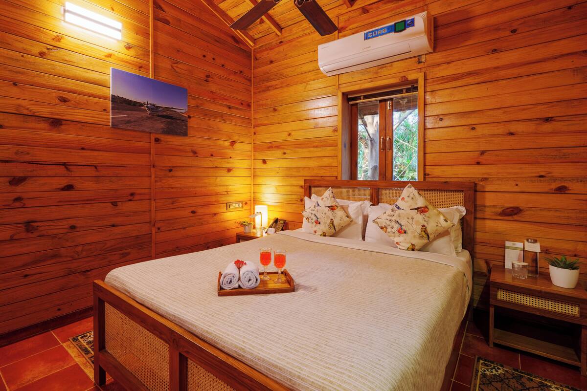 Une pièce de type cabane en bois, comprenant un lit, une table de chevet, une fenêtre et un climatiseur fixé au mur.