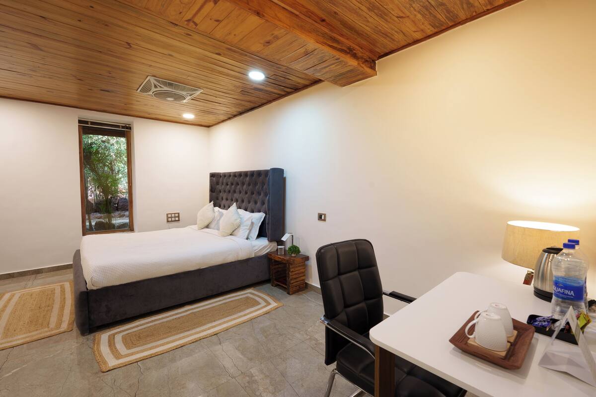 Une chambre avec un grand lit, un bureau avec une chaise, une lampe et une bouteille d’eau.