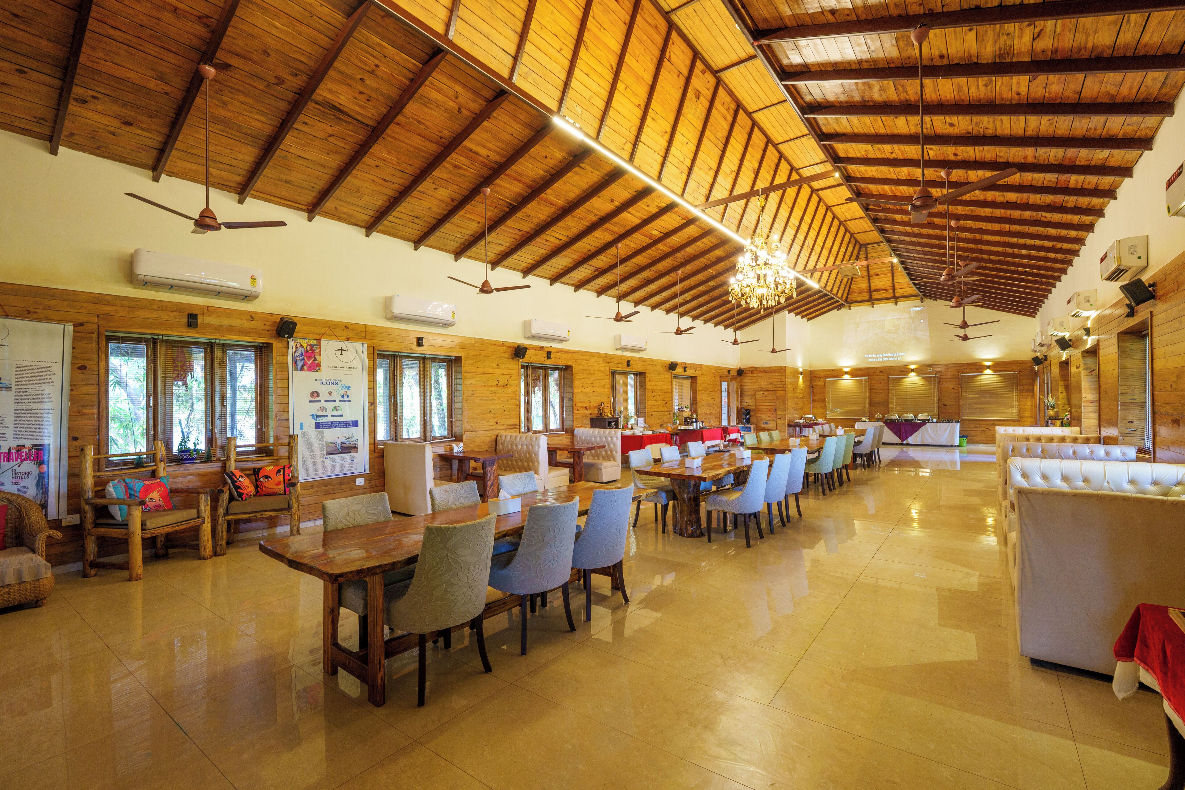 A spacious indoor dining area with wooden ceiling beams, multiple tables and chairs, and ceiling fans.