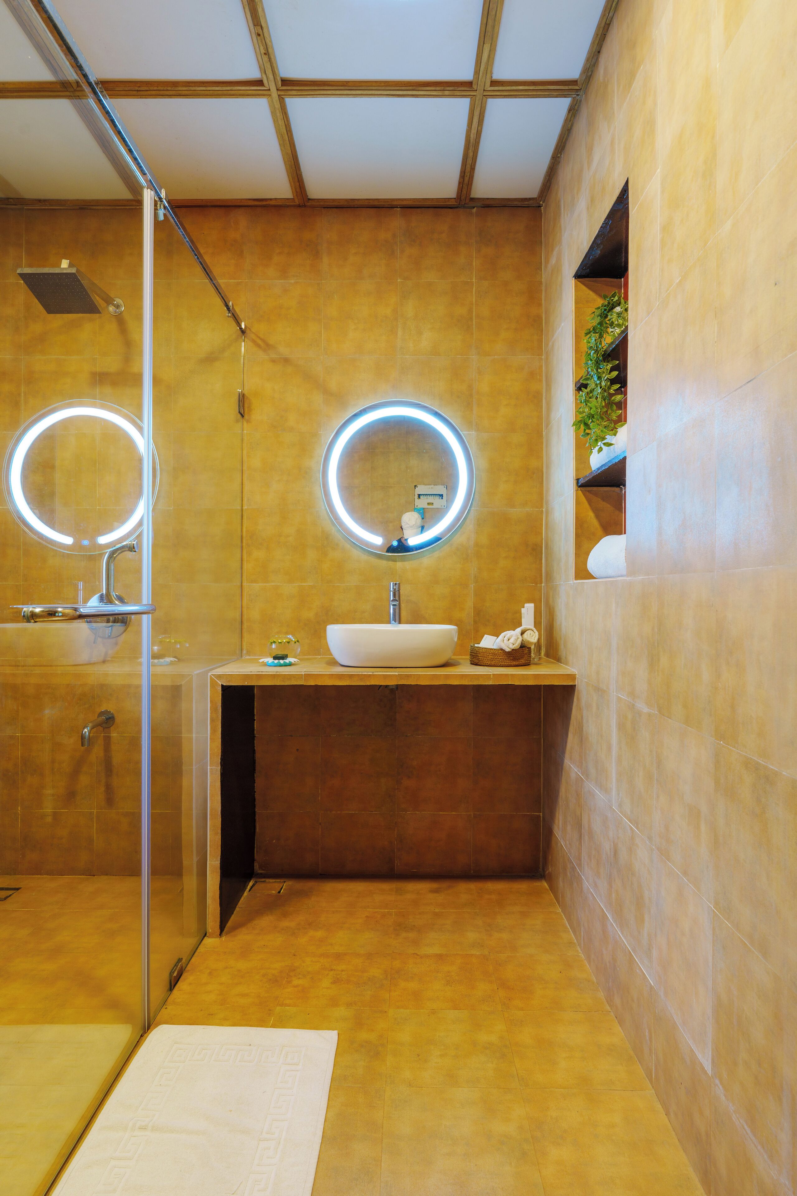 A modern bathroom with a glass-enclosed shower, a sink with a mirror, and a small shelf with toiletries.