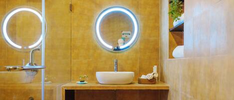 A modern bathroom with a glass-enclosed shower, a sink with a mirror, and a small shelf with toiletries.