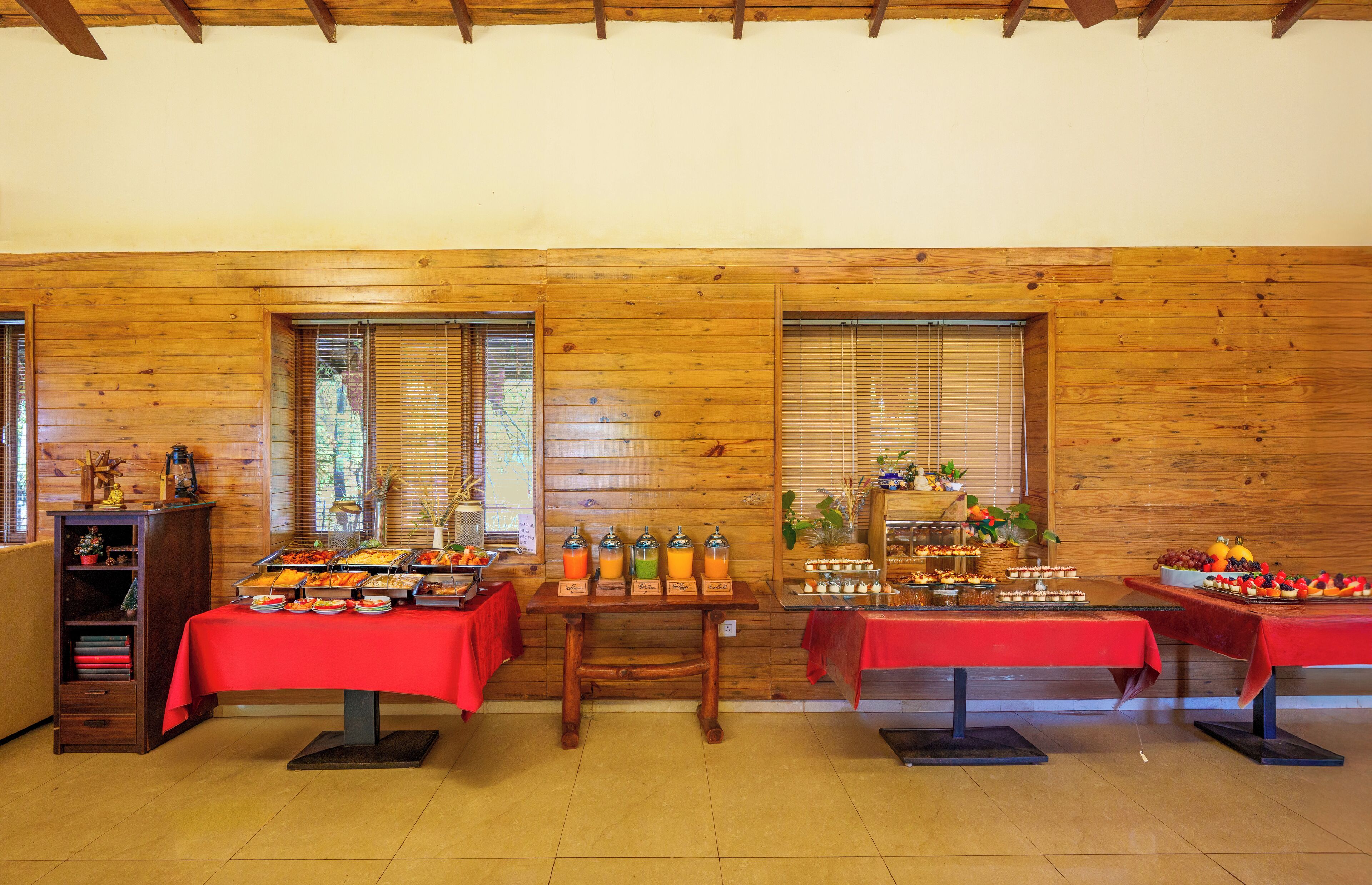 A buffet setup with various food items and beverages, wooden walls, and a red tablecloth.