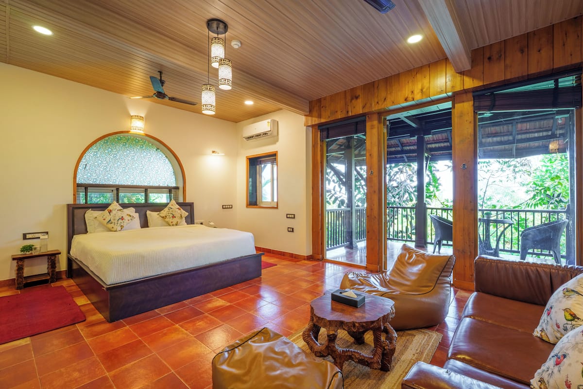 Une chambre avec un grand lit, un canapé, une petite table et un balcon avec des chaises.