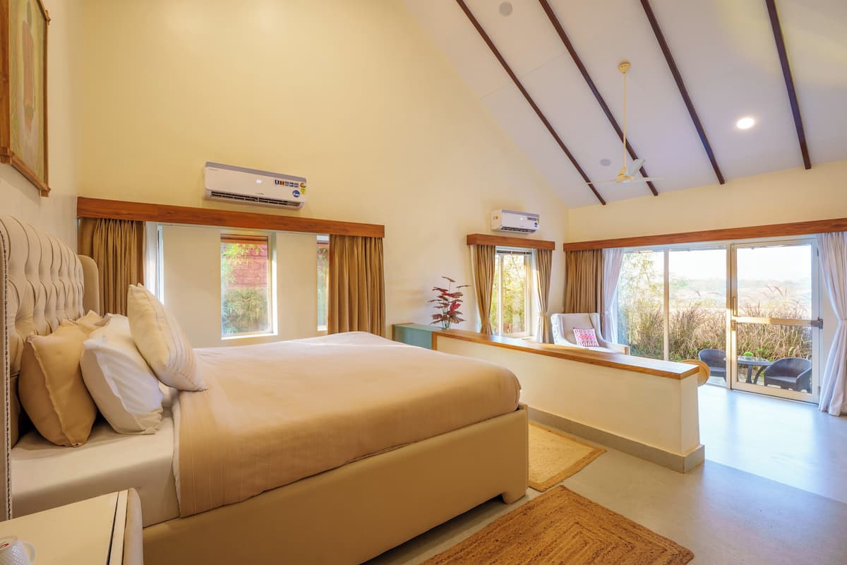 Une chambre dotée d’un grand lit, de deux climatiseurs, d’un ventilateur de plafond et offrant une vue sur l’extérieur grâce à de grandes fenêtres.