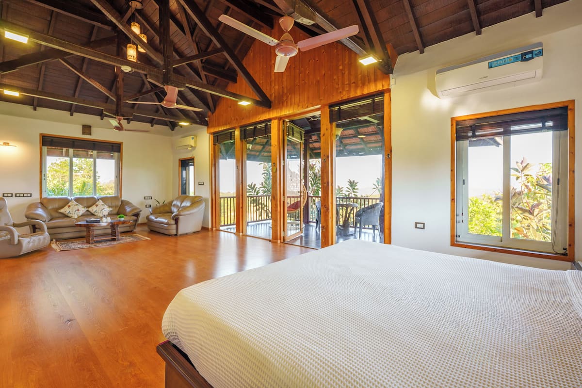 Une chambre spacieuse avec un grand lit, un coin salon avec des canapés et un balcon offrant une vue sur les palmiers.