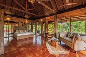 Una habitación amplia con una cama grande, un sofá y una mesita de centro. Cuenta con ventanas grandes y techo de madera.