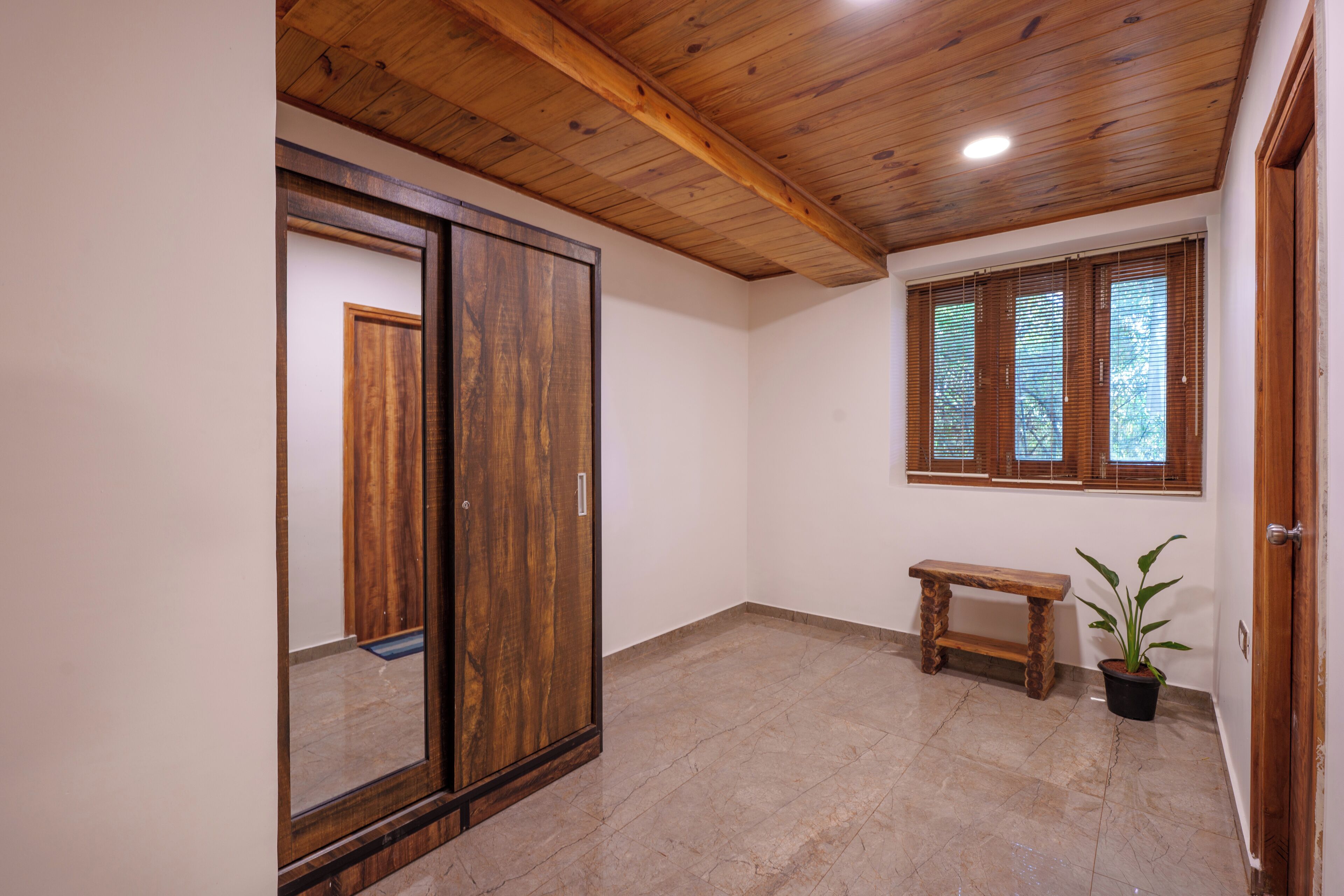 Een kamer met een houten plafond, een grote garderobe, een bankje en een potplant.