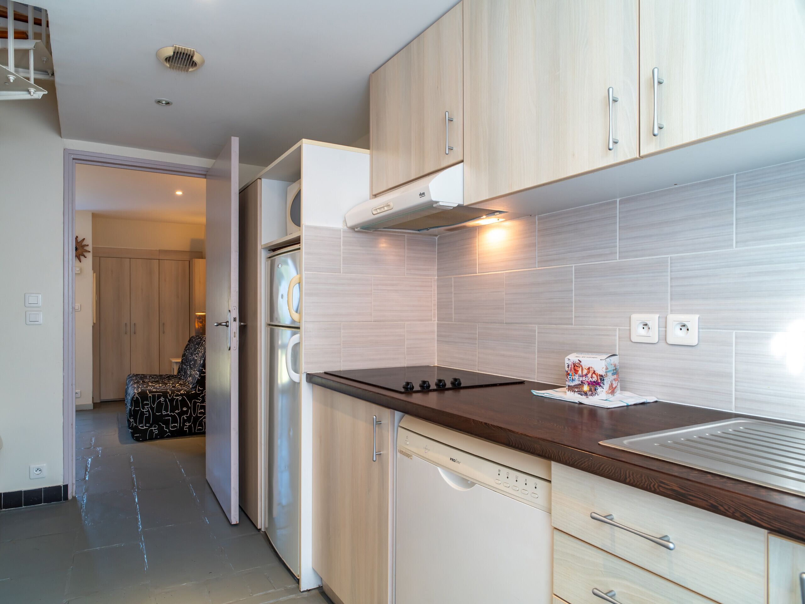 A modern kitchen with light wood cabinets, a stainless steel refrigerator, and a built-in dishwasher.