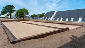 Un espacio amplio y abierto con suelo de arena, rodeado de árboles y un edificio con varios tejados inclinados.